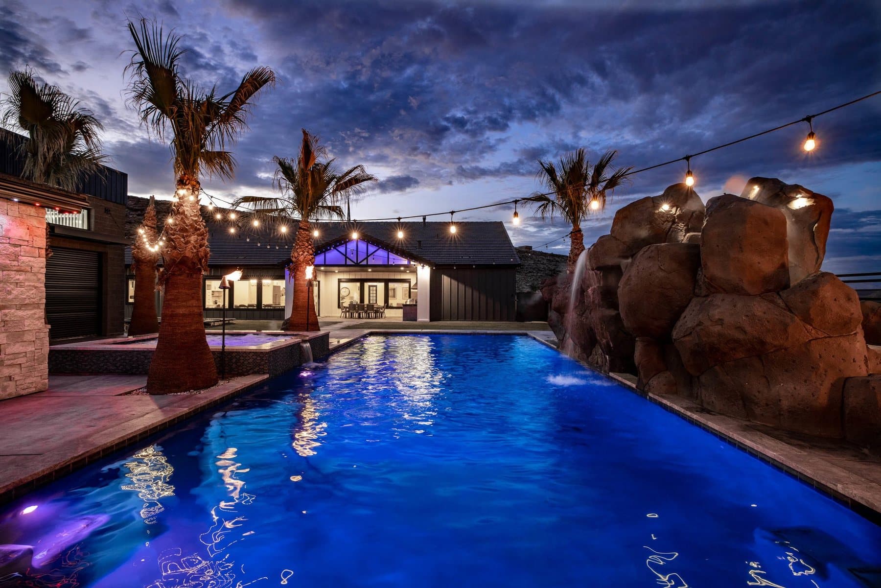 Crimson Shadows Estate at dusk — the sports pool leading to the lit house under palms and string lights